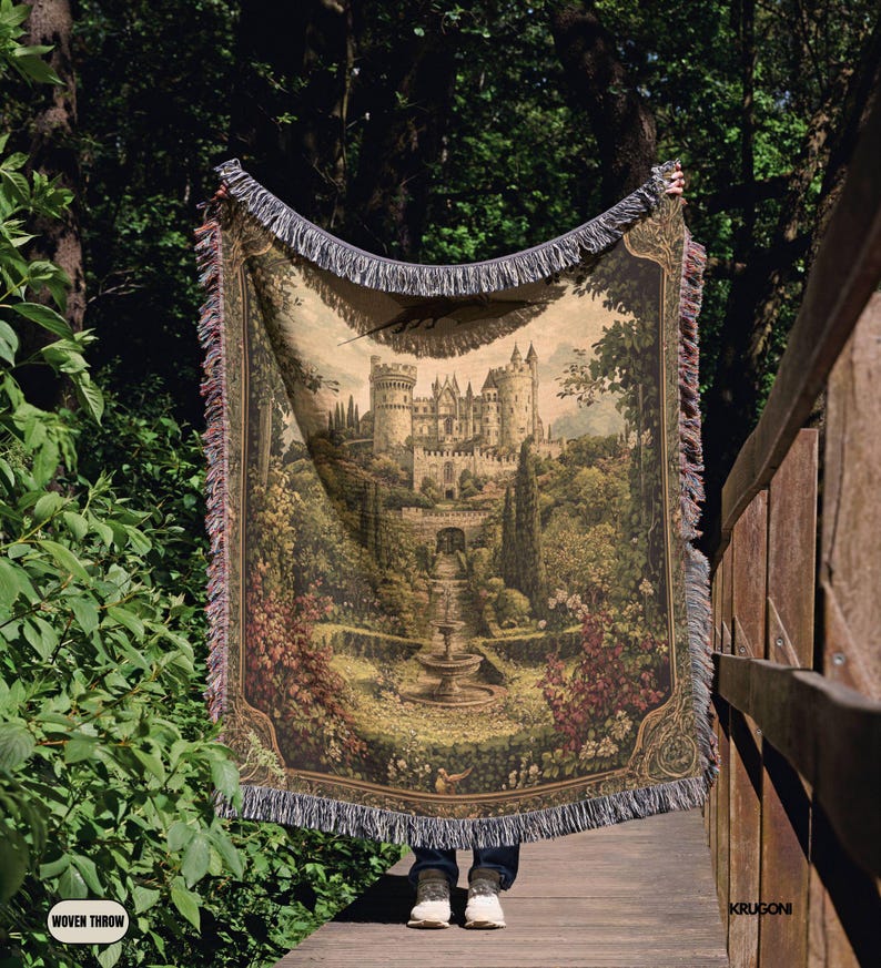 Pode incluir: Uma manta tecida com uma ilustra&ccedil;&atilde;o detalhada em estilo de tape&ccedil;aria de um castelo de pedra rodeado por jardins exuberantes, &aacute;rvores e uma fonte central. O tecido retangular tem bordas com franjas decorativas na parte superior e inferior.