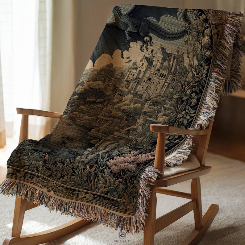 May include: A woven throw blanket featuring a detailed tapestry-style illustration of a large dragon flying over a stone castle and lush landscape. The blanket has a fringed edge and is draped over a wooden rocking chair with a light-colored seat.