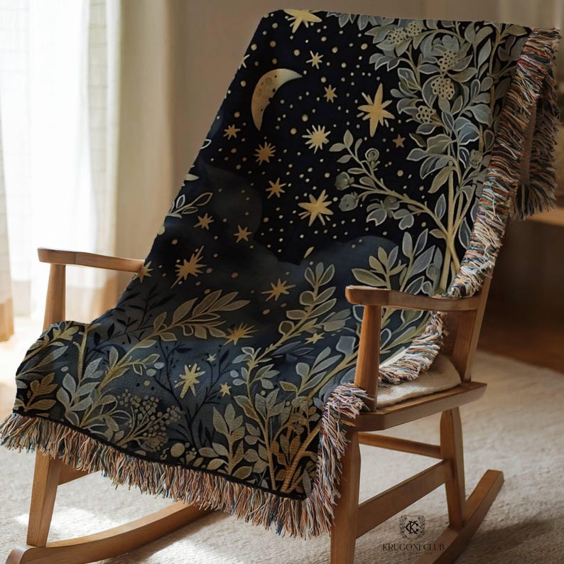 May include: A dark blue throw blanket draped over a wooden rocking chair. The blanket features a celestial design with a crescent moon, stars, and botanical elements in gold and green. The blanket has a fringed edge.