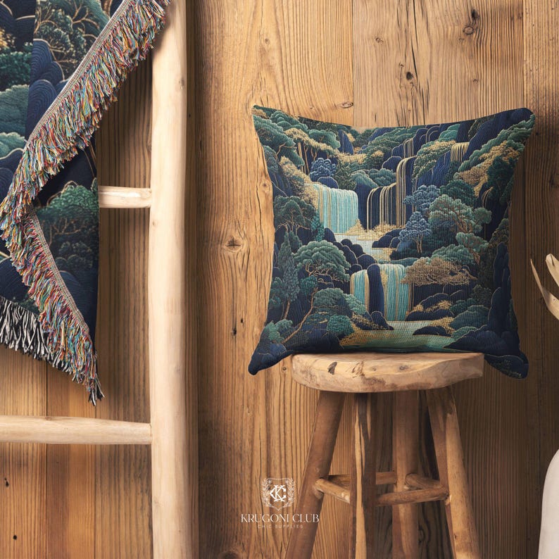 May include: A square decorative pillow with a waterfall landscape design in shades of blue, green, and gold. The pillow is placed on a small wooden stool. A matching throw blanket with fringe is partially visible.