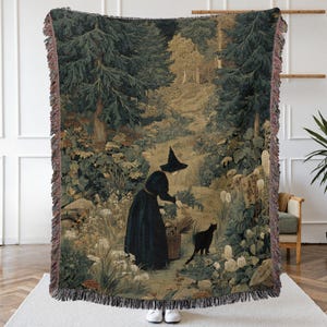 May include: Woven throw blanket featuring a forest scene with a figure in a black dress and hat, a black cat, and a basket. The blanket has a fringed edge with shades of green, brown, and beige. The artwork depicts a witch in a forest.