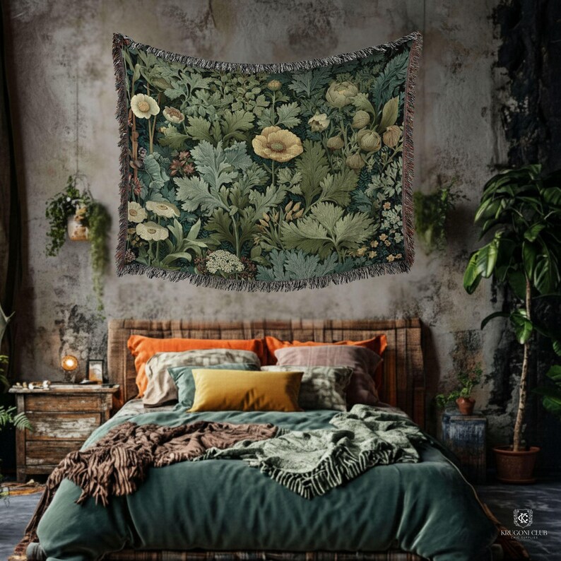 A rustic bohemian bedroom with a tropical green William Morris botanical tapestry hanging above the bed, featuring monstera leaves and muted yellow  flowers. The space includes a textured concrete wall, earthy bedding in green, rust, and terracotta tones, hanging plants, and lush potted greenery for a cozy indoor jungle vibe.