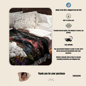 May include: A woven throw blanket featuring a dark, detailed illustration of a dragon resting on books amidst colorful flowers. The blanket has a black background with red, purple, and yellow floral accents. It is displayed on a bed with pillows.
