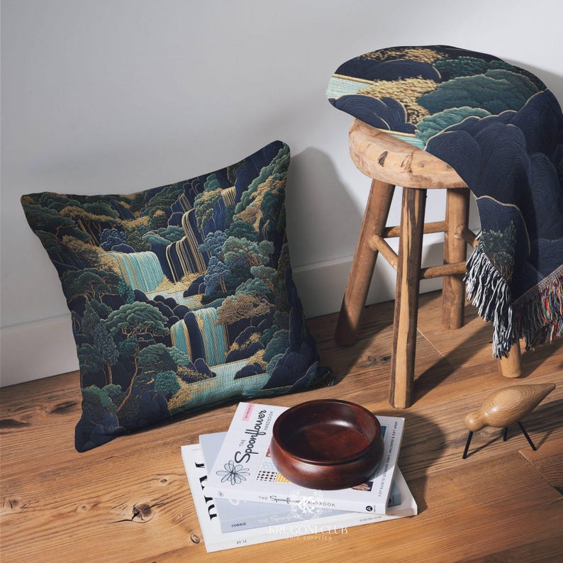 May include: A decorative pillow with a waterfall landscape design in shades of blue, green, and gold. A matching throw blanket is draped over a wooden stool. A wooden bowl and books are on the floor.
