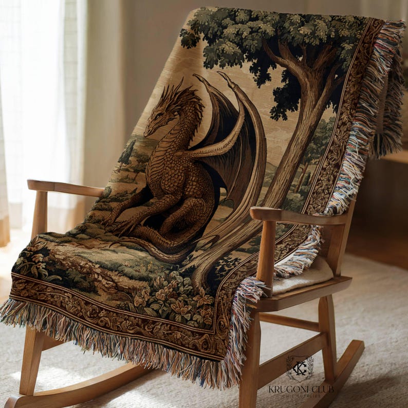 May include: A woven tapestry throw blanket featuring a detailed illustration of a dragon with outstretched wings, set against a backdrop of a tree and landscape. The blanket has a fringed edge and is draped over a wooden rocking chair.