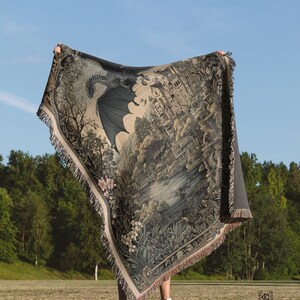 May include: A woven throw blanket featuring a detailed illustration of a large dragon flying over a castle, a lake, and lush foliage. The tapestry-style blanket has a fringed edge and displays a muted color palette of dark greens, browns, and creams.