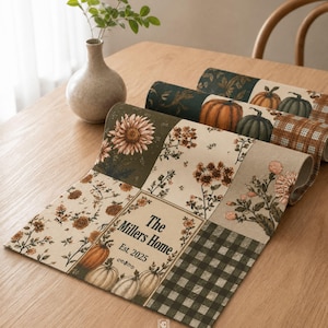 Puede incluir: Un camino de mesa rectangular de tela con un diseño de patchwork que incluye motivos florales, calabazas y un estampado de cuadros vichy en verde oscuro. El panel central muestra el texto "The Millers Home Est. 2025" enmarcado por ilustraciones botánicas.