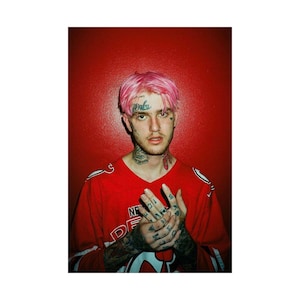 May include: A man with pink hair and tattoos is wearing a red jersey with white trim. He is standing in front of a red background.