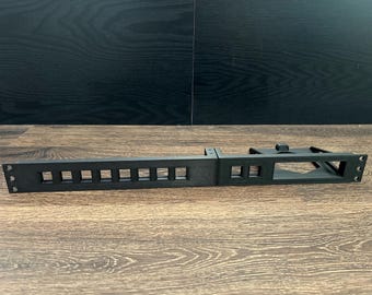 May include: Black plastic rack with 10 square openings and a rectangular opening. The rack is designed for mounting in a server rack.