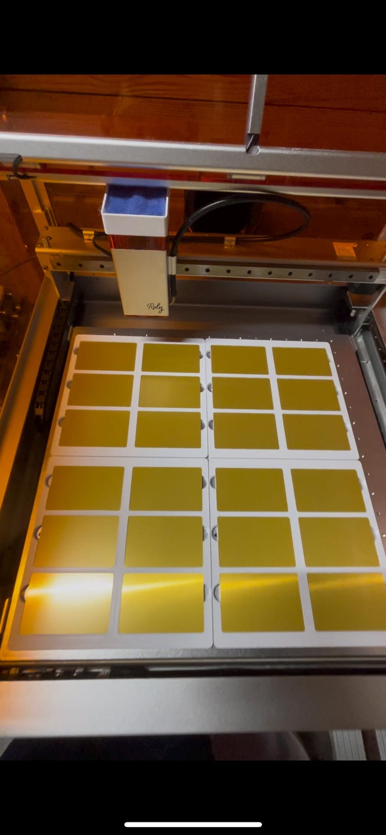 May include: A close-up of a laser cutting machine with a sheet of gold-colored material being cut into 12 rectangular pieces. The machine is labeled "Rolz".