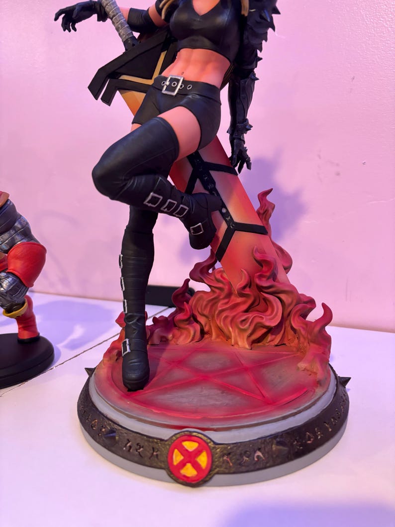 May include: A detailed figurine of a female character in a dynamic pose, clad in a black outfit with knee-high boots. The figure stands on a base with a fiery, orange and red design, and a circular emblem.