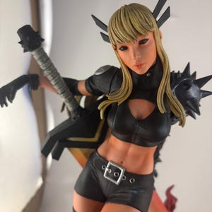 May include: A detailed figurine of a female character with blonde hair, wearing a black outfit with a cut-out top, shorts, and boots. The figure is holding a weapon and has black accents. The figurine has a dynamic pose and is set against a neutral background.