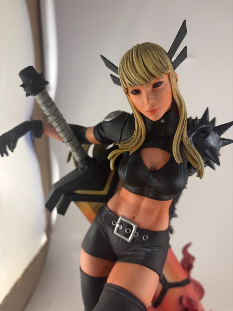 May include: A detailed figurine of a female character with blonde hair, wearing a black outfit with a cut-out top, shorts, and boots. The figure is holding a weapon and has black accents. The figurine has a dynamic pose and is set against a neutral background.