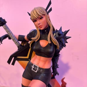 May include: A detailed figurine of a female character with blonde hair, wearing a black outfit with spiked shoulder armor and holding a black guitar. The figure has a determined expression and is posed dynamically.