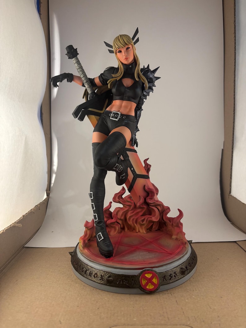 May include: A detailed figurine of a female character in a black outfit, holding a weapon. The figure stands on a base with a fiery design and an X-Men logo. The character has blonde hair and is in a dynamic pose.