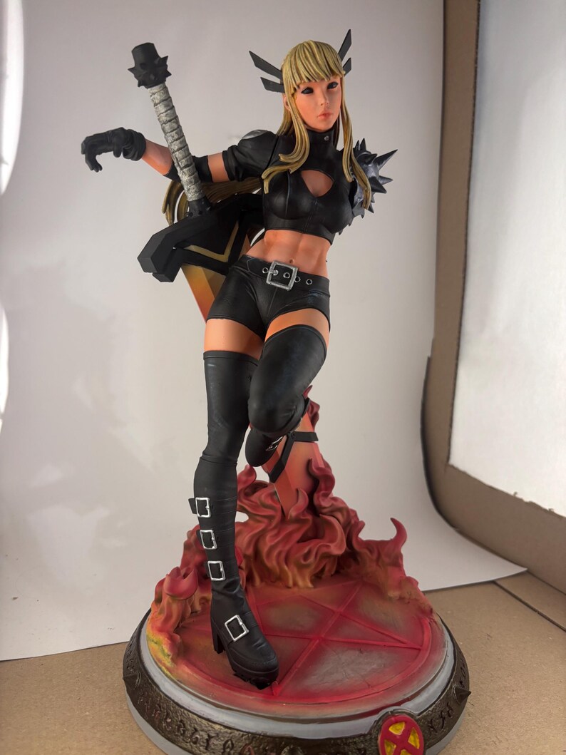 May include: A detailed figurine of a female character in a dynamic pose, holding a stylized weapon. She wears a black outfit with thigh-high boots and a belt. The base features a fiery design with a red pentagram and the X-Men logo.