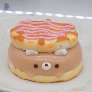 K&ouml;nnte beinhalten: Ein runder Kuchen, der wie ein Igel dekoriert ist. Der Kuchen ist mit rosa Zuckerguss &uuml;berzogen und hat ein braunes Gesicht mit wei&szlig;en Augen und einer schwarzen Nase.