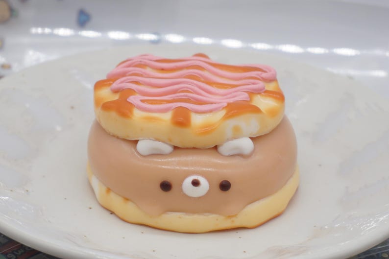 K&ouml;nnte beinhalten: Ein runder Kuchen, der wie ein Igel dekoriert ist. Der Kuchen ist mit rosa Zuckerguss &uuml;berzogen und hat ein braunes Gesicht mit wei&szlig;en Augen und einer schwarzen Nase.