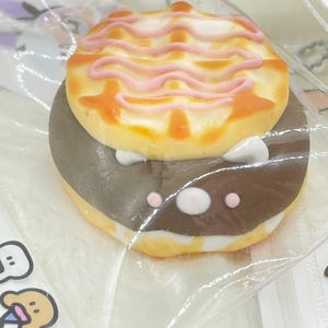 K&ouml;nnte beinhalten: Nahaufnahme eines Schokoladen-Waffel-Kekses mit rosa Zuckerguss. Der Keks ist in Klarsichtfolie verpackt und hat einen wei&szlig;en Hintergrund.