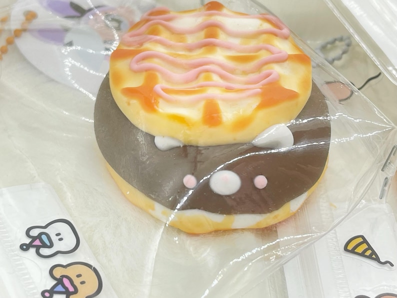K&ouml;nnte beinhalten: Nahaufnahme eines Schokoladen-Waffel-Kekses mit rosa Zuckerguss. Der Keks ist in Klarsichtfolie verpackt und hat einen wei&szlig;en Hintergrund.