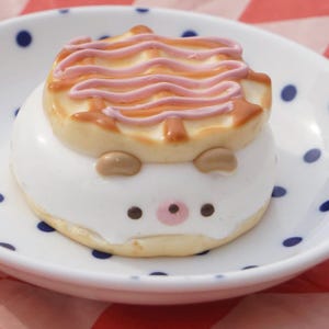 K&ouml;nnte beinhalten: Ein wei&szlig;er und brauner Kuchen in Form eines Igels mit rosa Zuckerguss auf der Oberseite, der auf einem wei&szlig;en Teller mit blauen Punkten liegt.