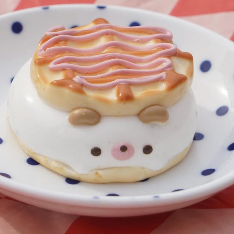 K&ouml;nnte beinhalten: Ein wei&szlig;er und brauner Kuchen in Form eines Igels mit rosa Zuckerguss auf der Oberseite, der auf einem wei&szlig;en Teller mit blauen Punkten liegt.
