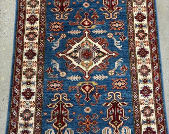 May include: A blue and red patterned rug with a central diamond design. The rug has a cream-colored border with intricate floral patterns.