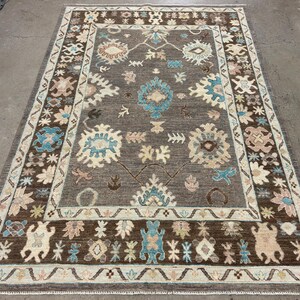 May include: A brown and beige area rug with a geometric pattern in shades of blue, brown, and beige. The rug has a border with a floral design.