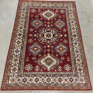 May include: A red, cream, and blue patterned rug with a traditional design. The rug has a central medallion and a border with intricate details.