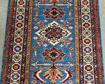 May include: A traditional blue and red rug with a geometric pattern. The rug has a central medallion with a floral design and a border with a repeating pattern.