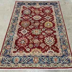 May include: A red, blue, and cream colored rug with a floral pattern. The rug has a detailed border with intricate designs.