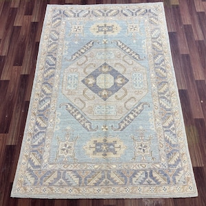 Könnte beinhalten: Ein hellblauer Teppich mit einem beige-braunen geometrischen Muster. Der Teppich hat ein traditionelles Design mit einem zentralen Medaillon und einem Rand.