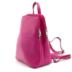 May include: A fuchsia-colored leather backpack with silver zippers and adjustable straps. The bag has a top handle and a structured design. The leather has a textured appearance, and the bag is set against a white background.