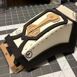 May include: A white foam model of a suit jacket with black foam trim. The jacket has a brown paper insert with the number "12" on it. The model is numbered "1", "2", and "3" on the sides.