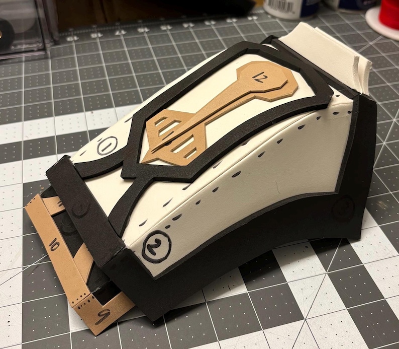 May include: A white foam model of a suit jacket with black foam trim. The jacket has a brown paper insert with the number "12" on it. The model is numbered "1", "2", and "3" on the sides.