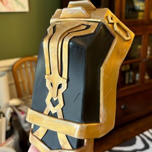 May include: A black and gold decorative piece with intricate details. The piece is made of a hard material and has a smooth, polished finish.