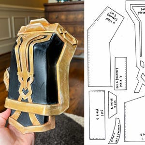 May include: A black and gold costume piece with intricate details. The piece is made of foam and has a textured surface. The piece is designed to be worn on the arm.