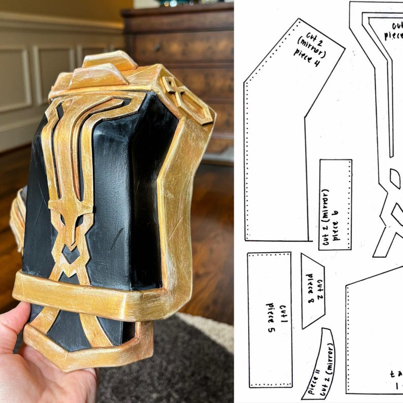 May include: A black and gold costume piece with intricate details. The piece is made of foam and has a textured surface. The piece is designed to be worn on the arm.