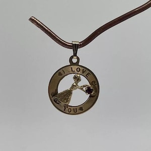 以下が含まれることがあります： 赤いハートを持った女性と「I LOVE YOU」の文字が刻まれた丸いチャームが付いたゴールドのネックレスです。