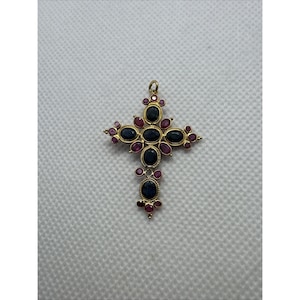 Puede incluir: Un colgante de cruz de oro con cinco zafiros azul oscuro de forma ovalada en el centro y los brazos, acentuado por numerosos rubíes rosas redondos pequeños dispuestos alrededor del perímetro y entre las piedras azules.