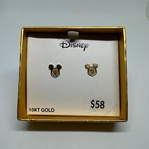 Pode incluir: Um par de brincos de Mickey Mouse de ouro em uma caixa branca com o logotipo da Disney e o texto "10KT GOLD" e "58 €".