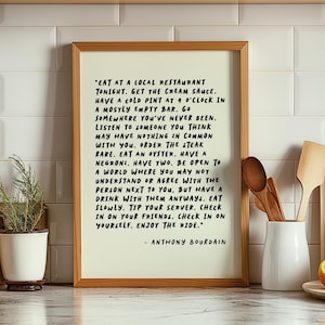 Peut inclure: Une affiche encadrée sur fond crème clair avec un texte noir écrit à la main : "Eat at a local restaurant tonight. Get the cream sauce. Have a cold pint at 4 o'clock in a mostly empty bar. Go somewhere you've never been. Listen to someone you think may have nothing in common with you. Order the steak rare. Eat an oyster. Have a negroni. Have two. Be open to a world where you may not understand or agree with the person next to you, but have a drink with them anyways. Eat slowly. Tip your server. Check in on your friends. Check in on yourself. Enjoy the ride." suivi de "- Anthony Bourdain".