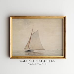 May include: A framed wall art print featuring a watercolor painting of a sailboat on the water. The sailboat has a tall mast and a large, light-colored sail. The scene is rendered in muted, neutral tones of beige, gray, and white.