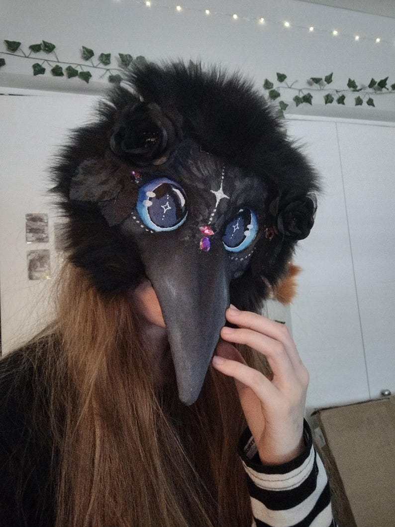 May include: A black plague doctor mask with a long, gray beak. The mask features large, blue eyes with star details, black roses, and a fluffy black fur trim. Decorative jewels are placed around the eyes. The mask is designed for cosplay or costume use.