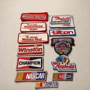 May include: A collection of embroidered fabric patches featuring various NASCAR and automotive racing logos, including Winston Racing Series, Raybestos, Tilton, and Champion, displayed in rectangular, shield, and custom shapes with red, white, blue, and black colors.