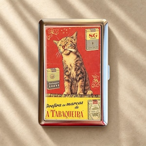 Puede incluir: Una pitillera rectangular de metal con un gráfico de estilo vintage de un gato atigrado con un cigarrillo en la boca. El diseño incluye tres ilustraciones de paquetes de cigarrillos y el texto "Prefira as marcas de A TABAQUEIRA" en rojo y negro.