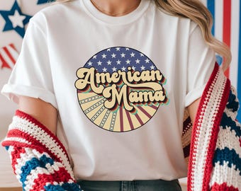 May include: White t-shirt with a retro design that says "American Mama" in a circular graphic. The graphic features a blue background with white stars, and a yellow and red sunburst design. The shirt is a casual style.
