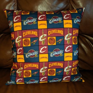 May include: A red, yellow, and blue throw pillow with a repeating pattern of the Cleveland Cavaliers logo and the word "Cleveland".