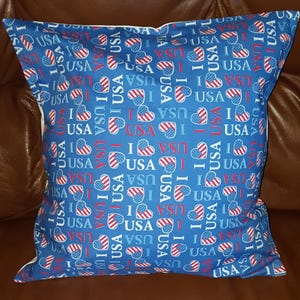 May include: Square blue pillow with a repeating pattern of red, white, and blue heart-shaped flags and the words "I USA". The pillow is a patriotic decorative item.