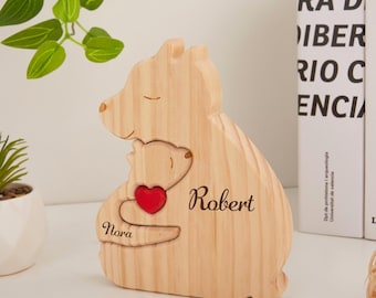 Puede incluir: Figura de madera con forma de oso, con un oso más pequeño abrazando un corazón rojo. Los nombres "Nora" y "Robert" están grabados en la figura. El oso es de madera clara.